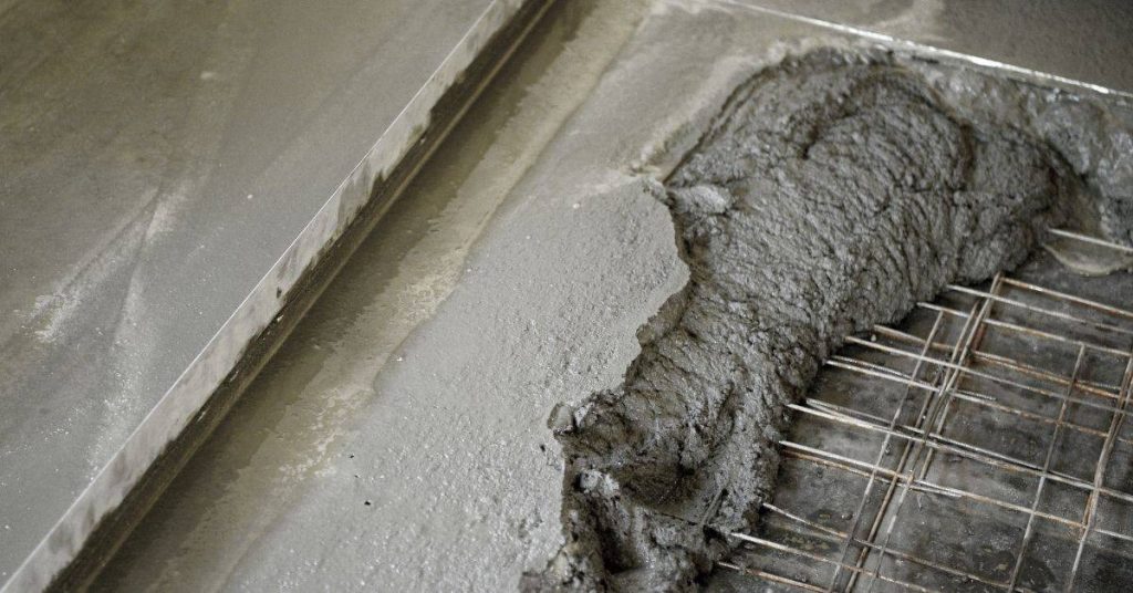 Wet concrete being poured over steel rebar grid