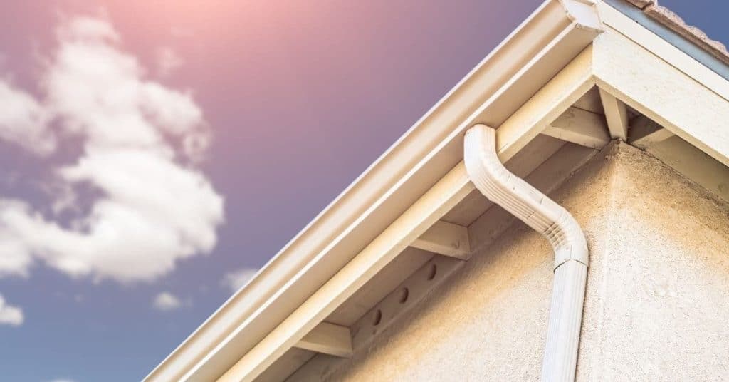 White gutter and downspout on beige house corner under blue sky