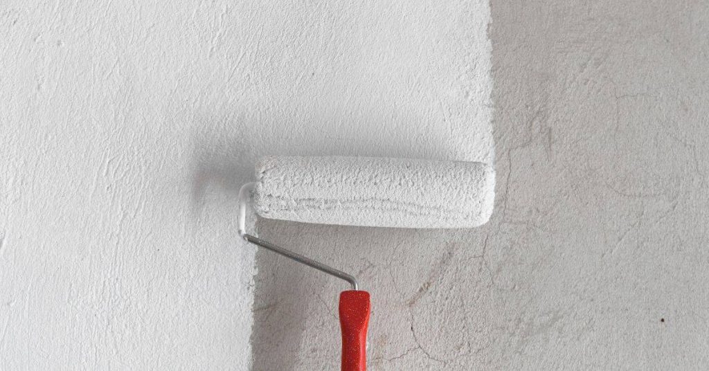 White paint roller applying paint on textured wall