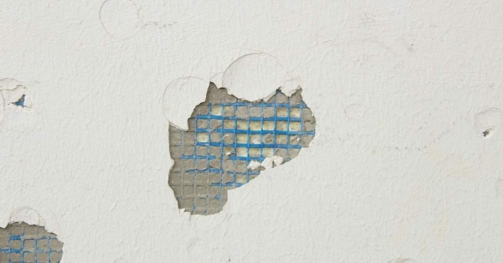 White stucco wall with damaged areas showing blue reinforcing mesh