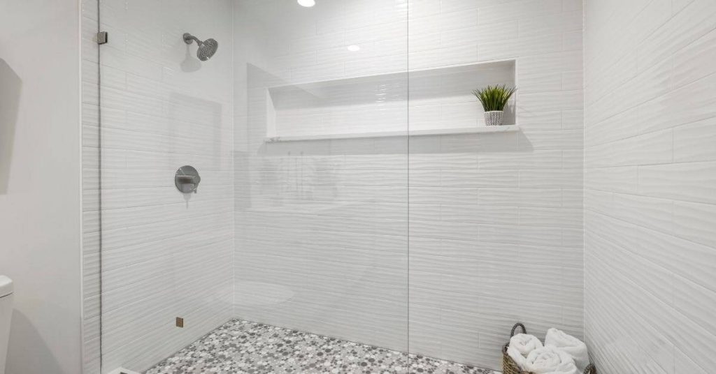 White textured wall tiles with glass shower enclosure and mosaic floor tiles