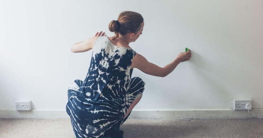 Woman in patterned dress cleaning white wall near floor