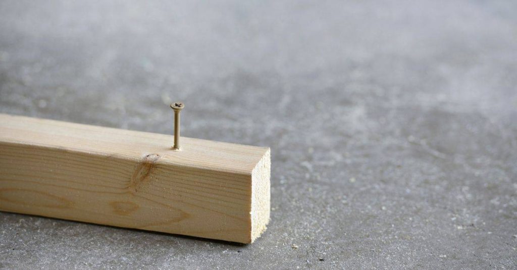 wood block with nail sticking out on concrete surface