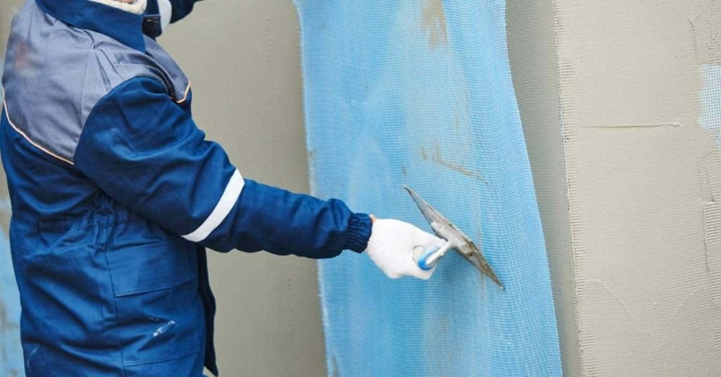 Worker applying plaster over blue reinforcing mesh on wall