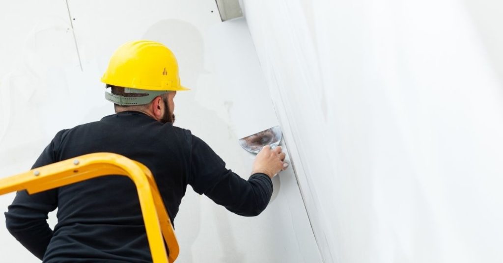 Worker applying plaster to a white wall wearing yellow helmet
