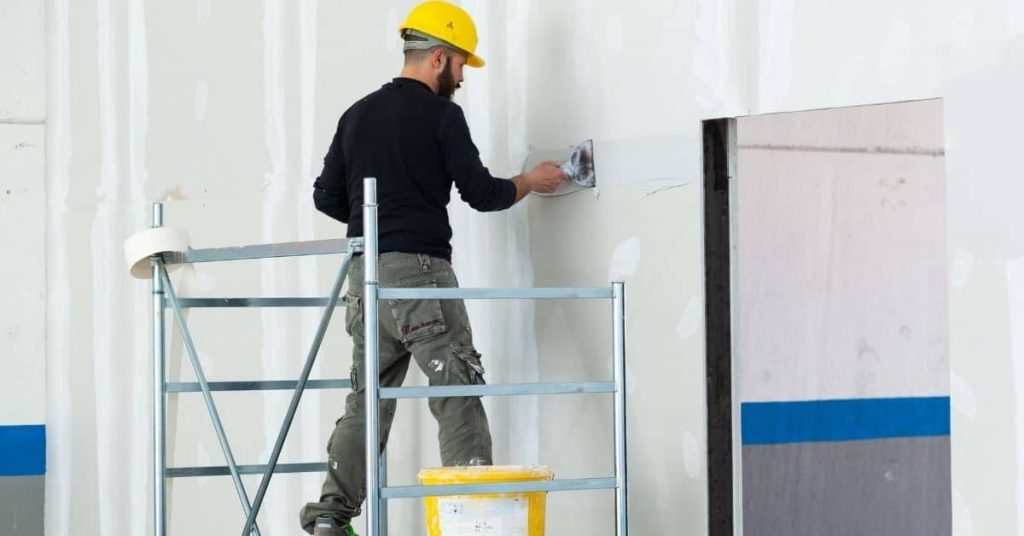 Worker applying plaster to drywall wearing yellow hard hat