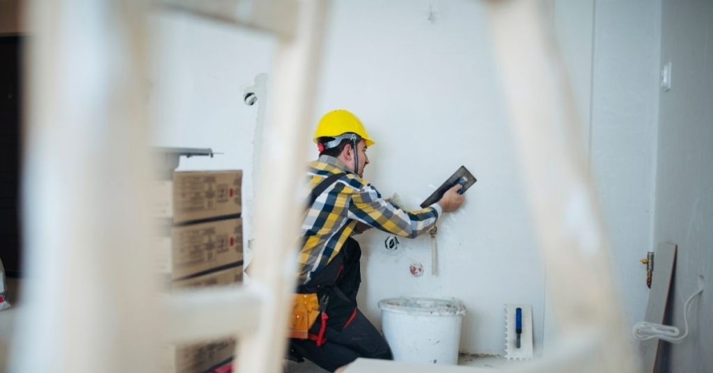 Worker applying plaster to interior wall wearing yellow safety helmet