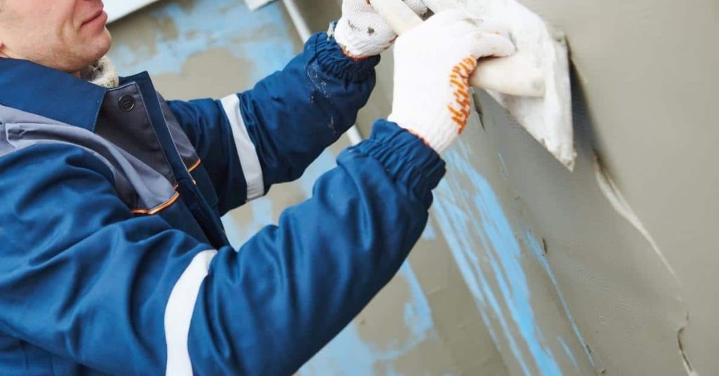 Worker applying stucco plaster onto wall with trowel