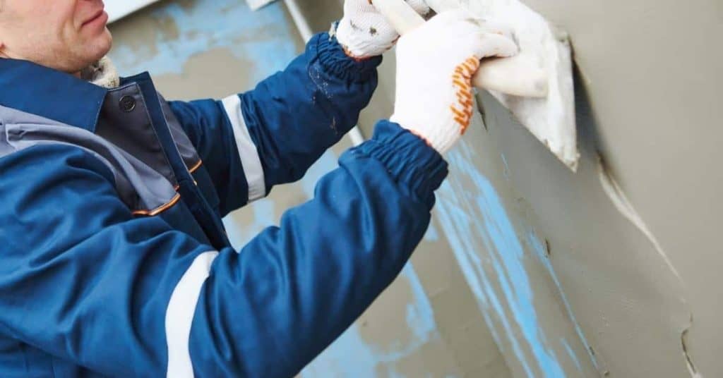 Worker applying stucco plaster with trowel on wall