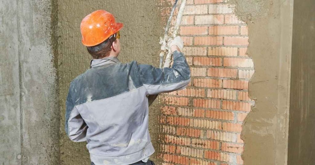 Worker applying stucco to brick wall wearing orange helmet