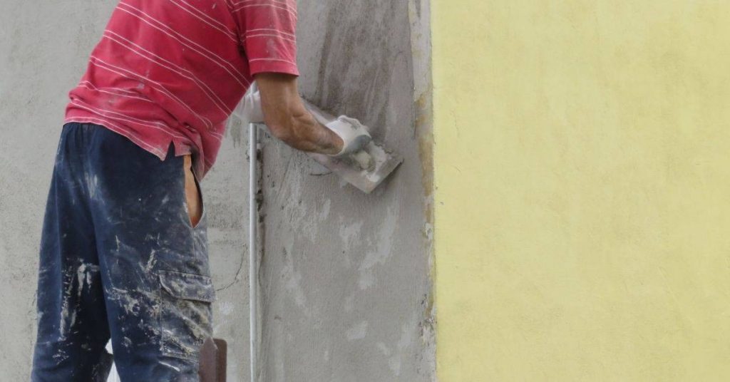 Worker applying wet stucco to wall with trowel