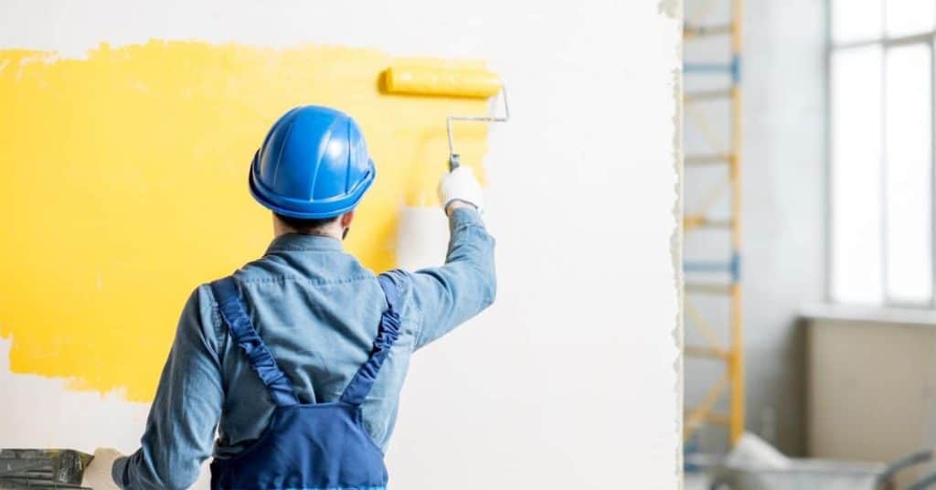 Worker in blue helmet painting wall yellow with roller