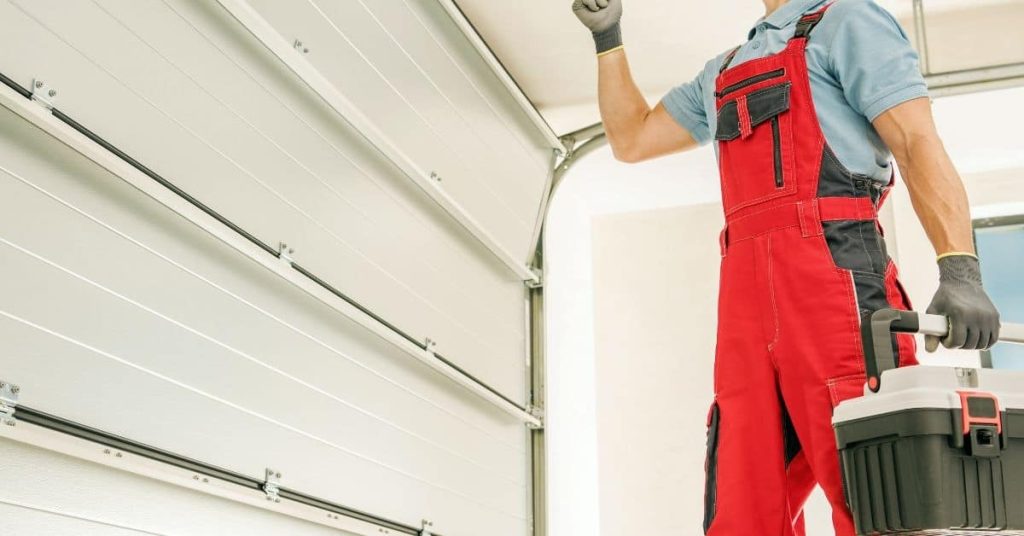 Worker in red overalls holding toolbox near garage door
