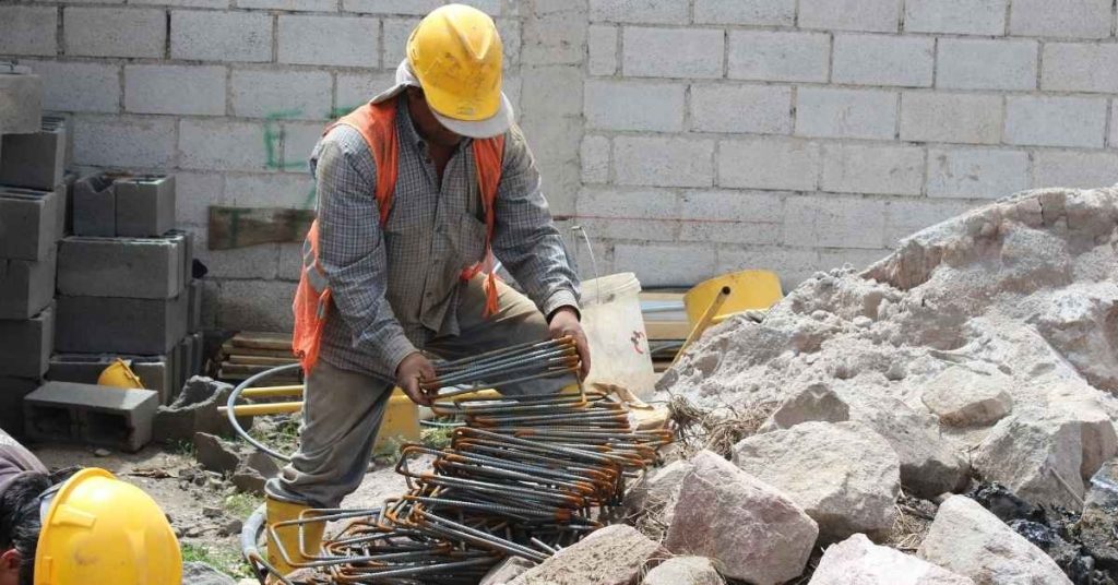 Worker in safety gear handling rusty rebar on construction site