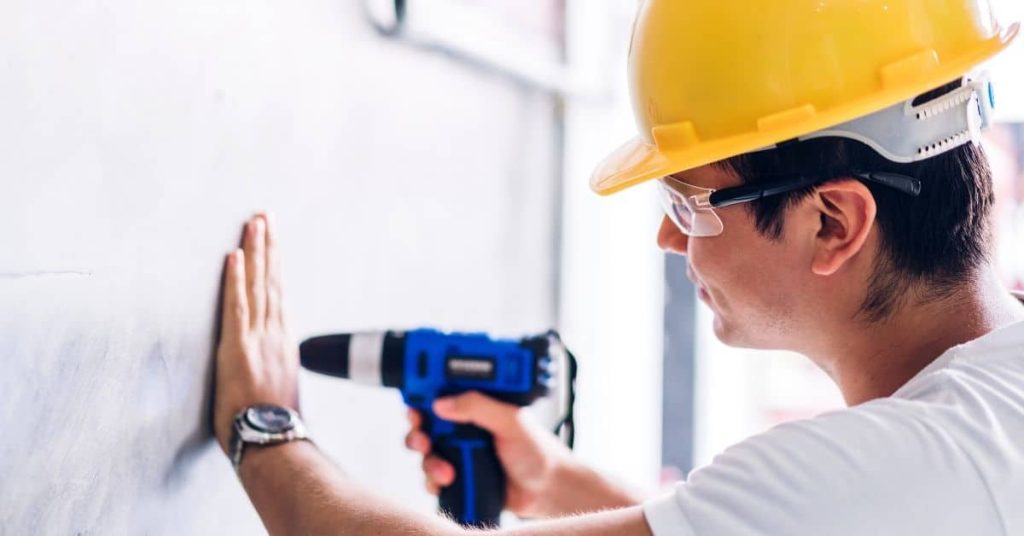 Worker in safety helmet holding drill near wall