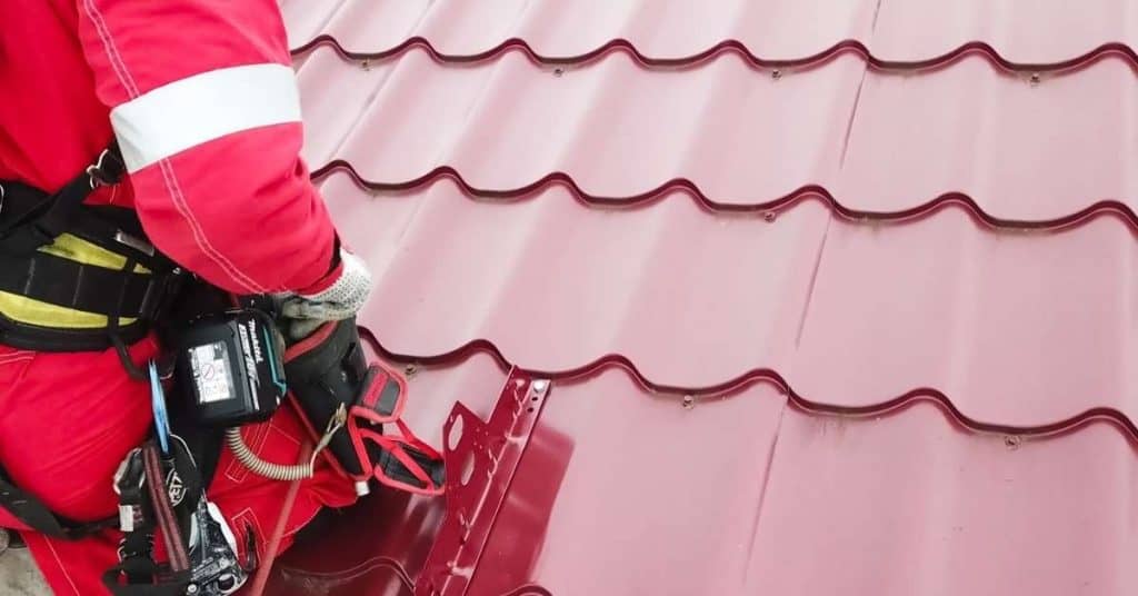 Worker installing metal roof fasteners on red metal panels