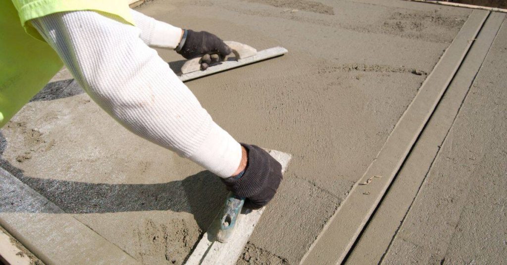 Worker smoothing fresh concrete with hand tools outdoors