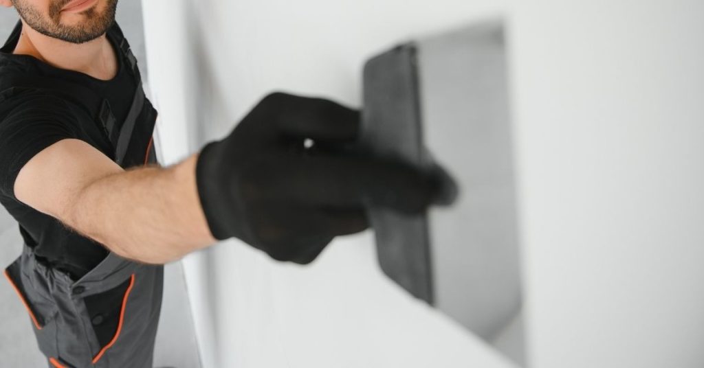 Worker smoothing plaster on wall with trowel