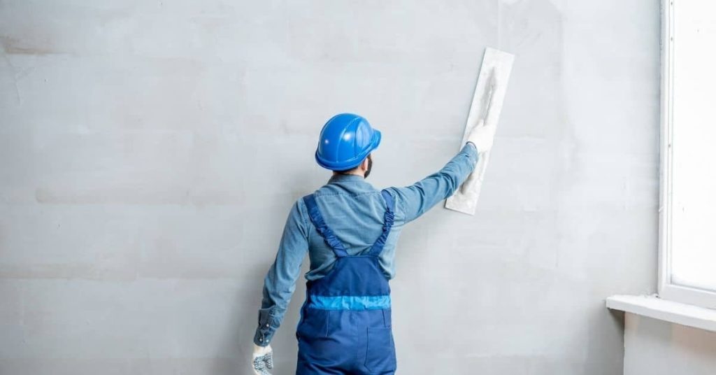 Worker smoothing plaster on wall with trowel