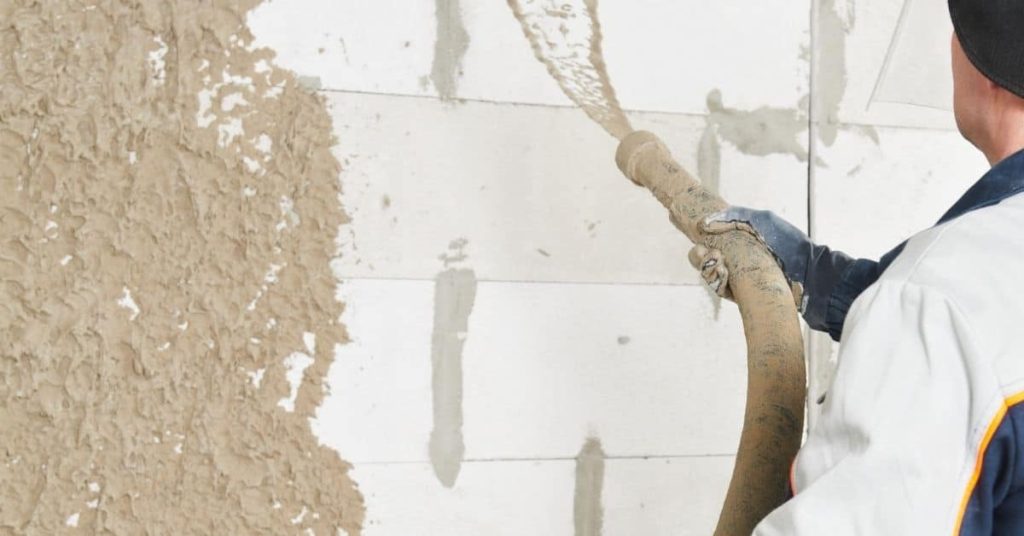 Worker spraying brown stucco on white wall