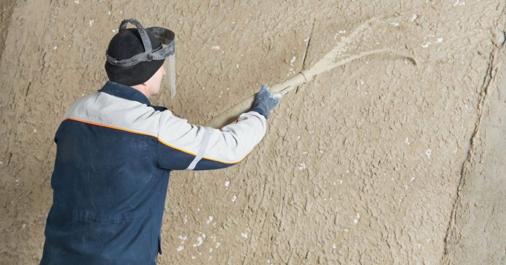 Worker spraying plaster onto wall wearing safety gear