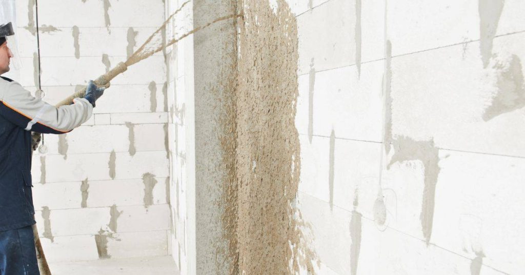 Worker spraying stucco onto concrete block wall