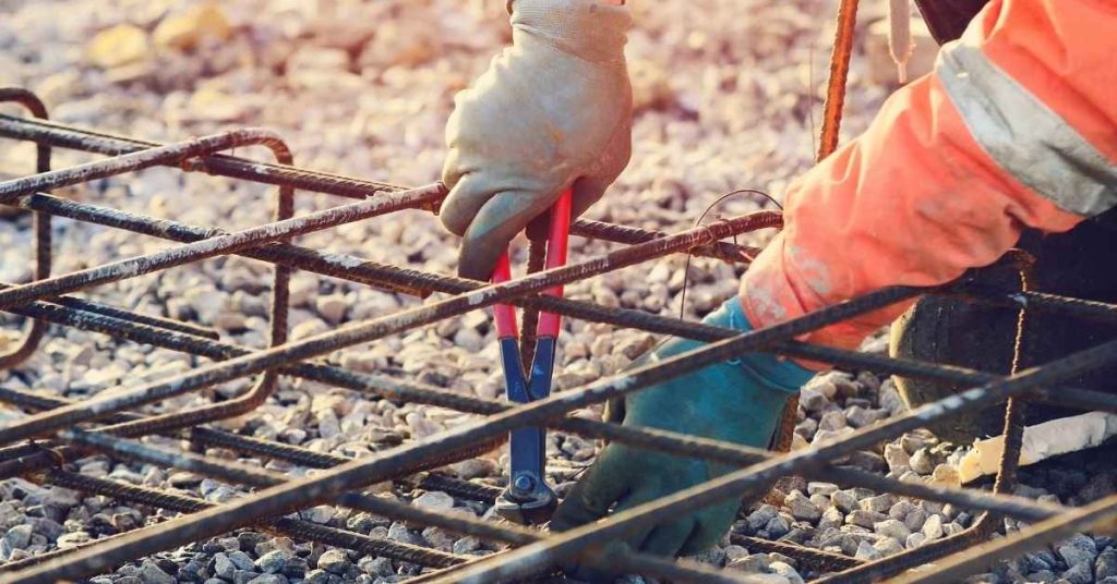 Worker tying rebar with pliers on gravel base