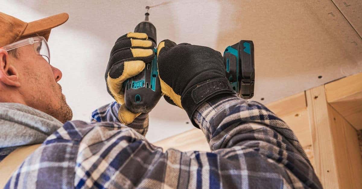 Worker wearing gloves using drill on ceiling drywall