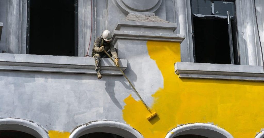 Worker wearing helmet painting exterior building yellow