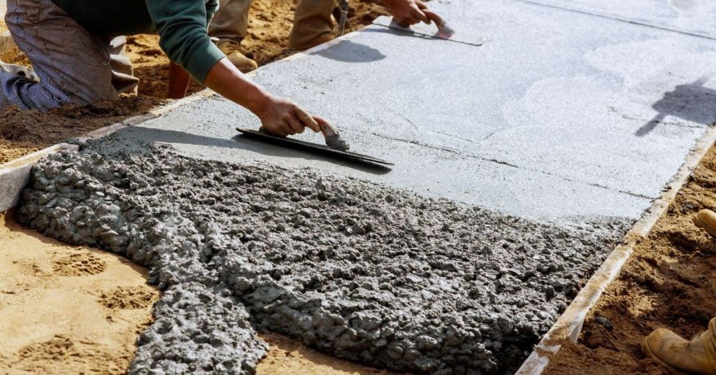 Workers finishing fresh concrete slab with hand trowels