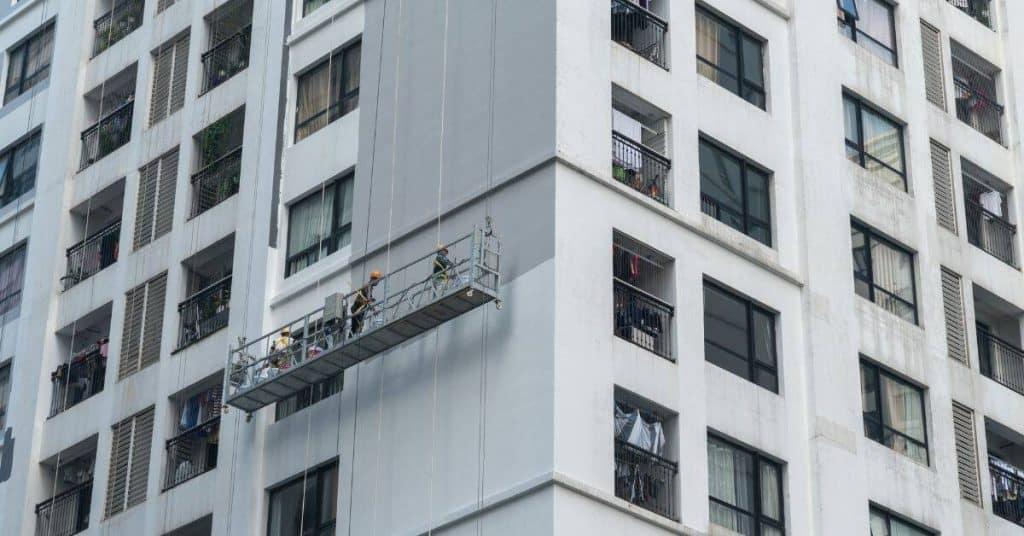 workers on suspended platform painting building exterior walls