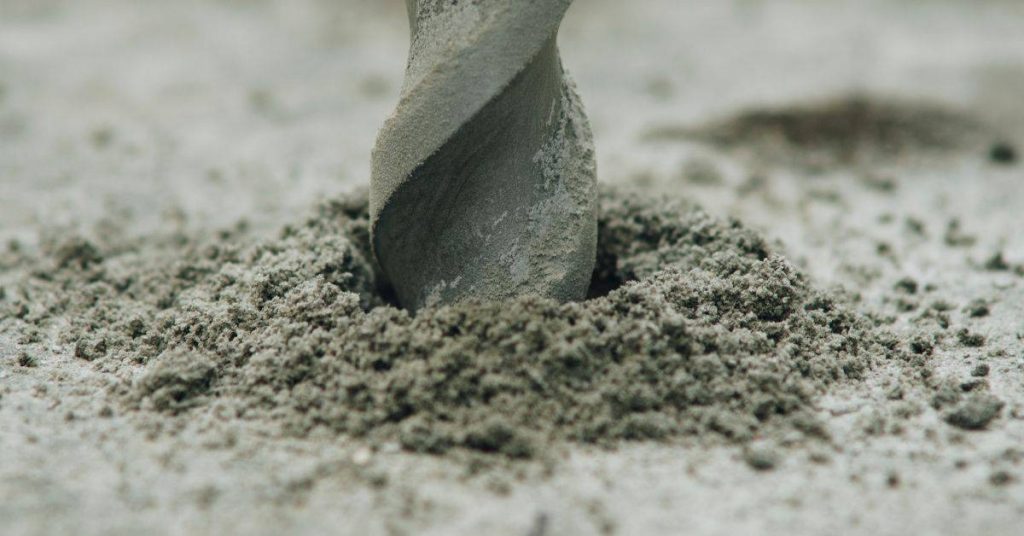 Close-up of a drill bit drilling into concrete with dust