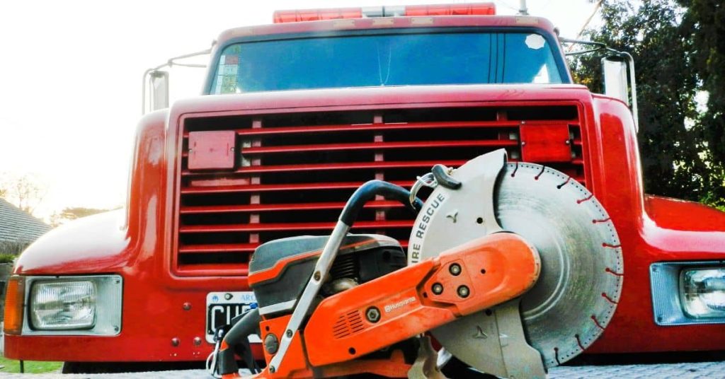 Close-up of red gas-powered cutting saw in front of vehicle
