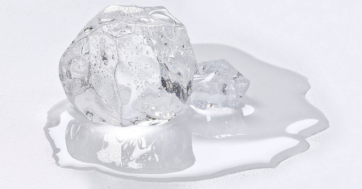 Two melting ice cubes with water puddle on white surface