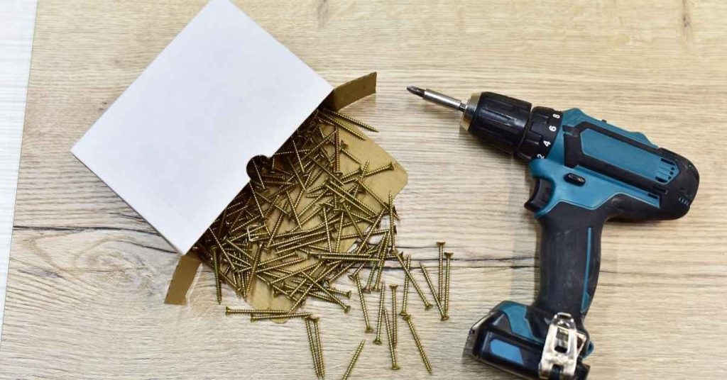Cordless drill and scattered wood screws on wooden surface