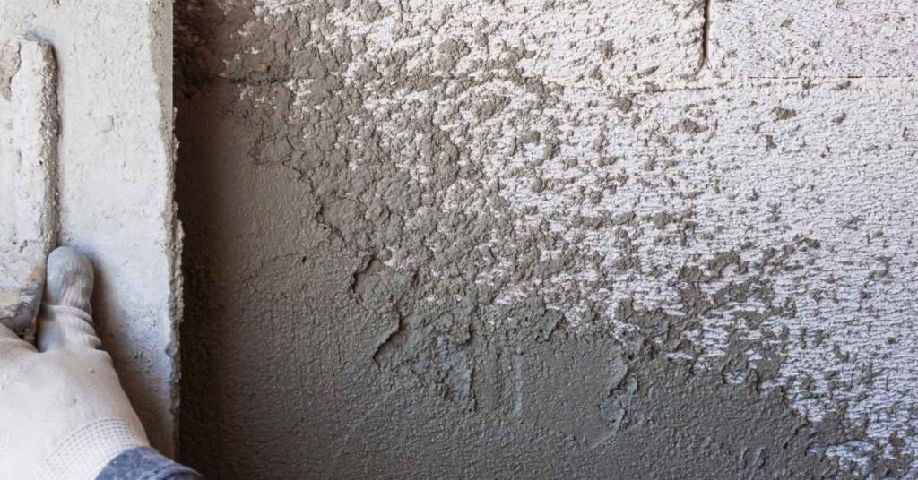 Gloved hand applying stucco scratch coat on lath