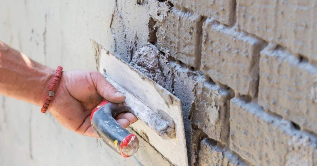 Hand applying plaster to brick wall with trowel