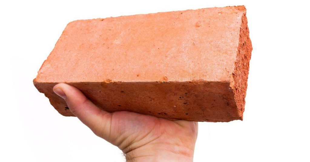 Hand holding a single red brick against white background