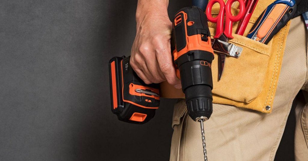 Hand holding cordless drill with tool belt on waist