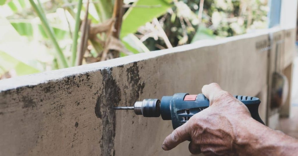 Hand holding drill against concrete wall surface