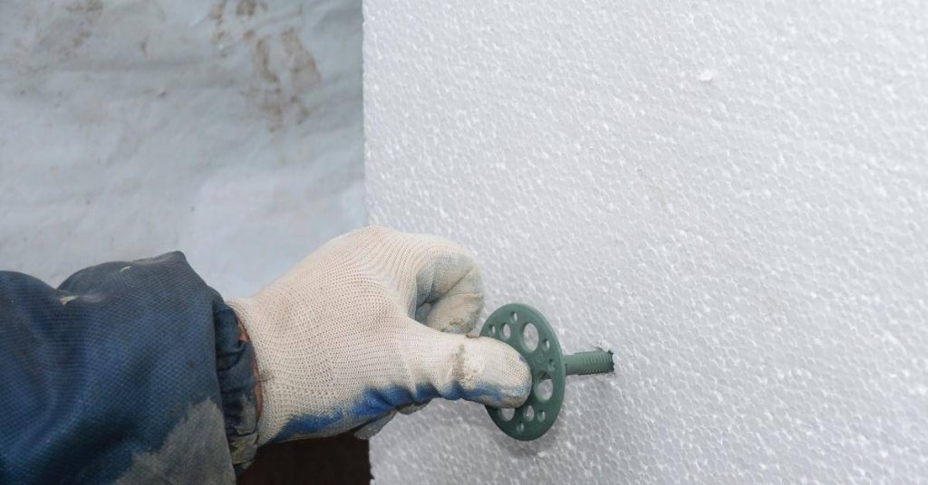 Hand with glove pushing plastic anchor into foam board insulation