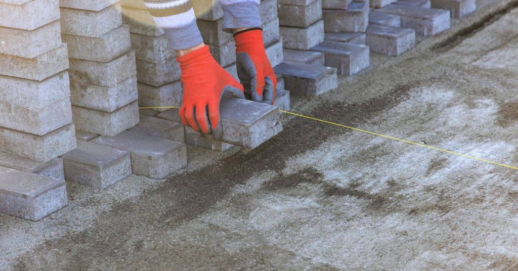 Hands wearing red gloves placing concrete block using string line