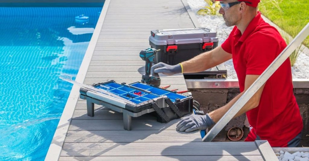 Man in red shirt working with toolbox and electric drill by pool