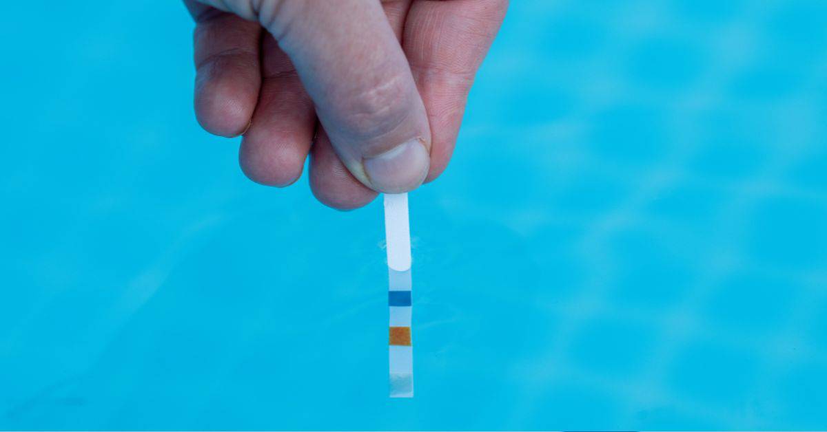 Hand holding chemical test strip above clear blue water