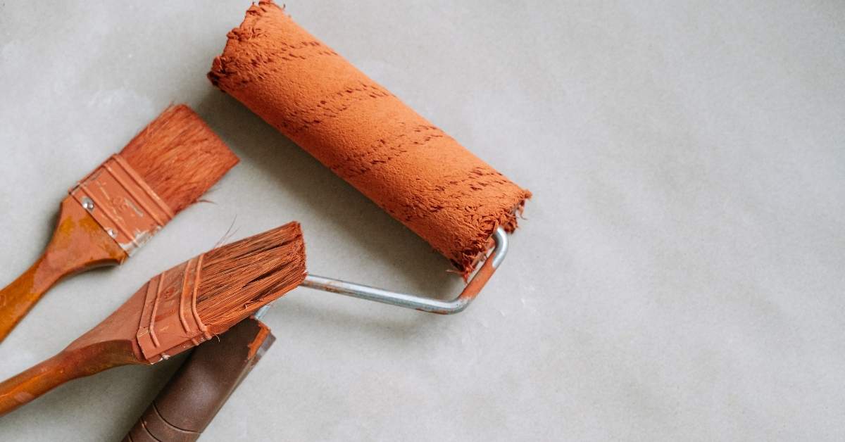 paint roller and brushes with reddish paint on gray surface