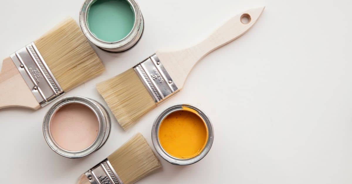 three paint brushes near open paint cans with teal yellow and pink paint