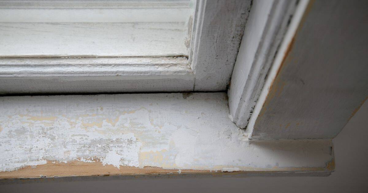 Peeling white paint on wooden window frame corner