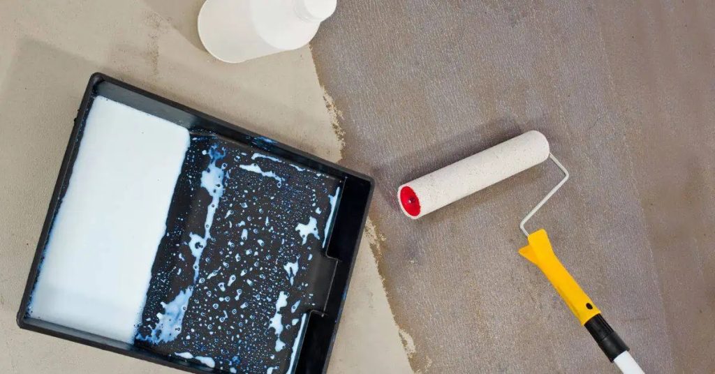 Paint roller and tray with white primer on concrete floor
