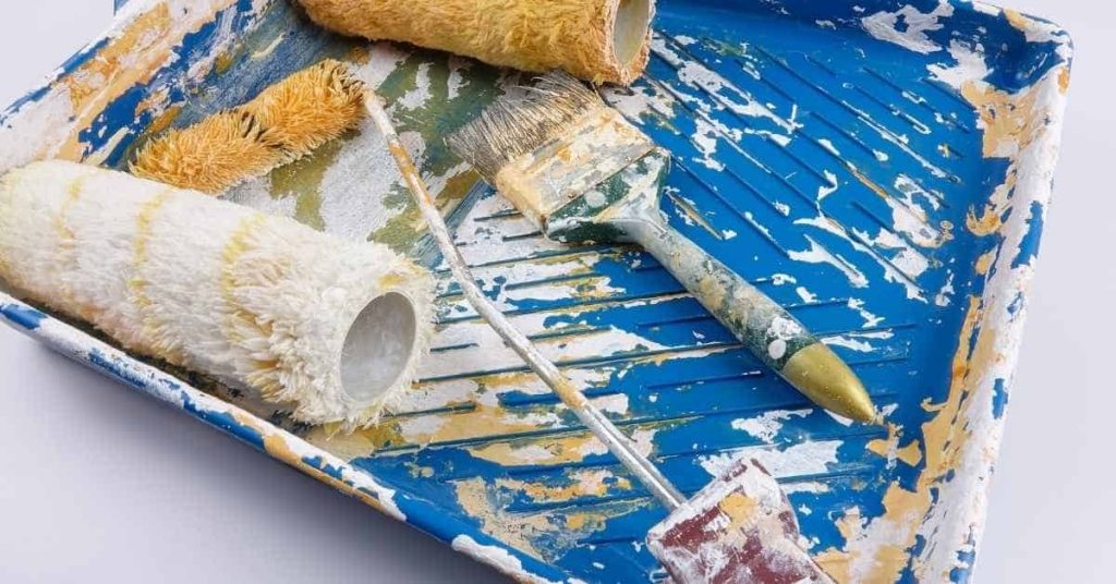 paint tray with rollers and brush covered in paint