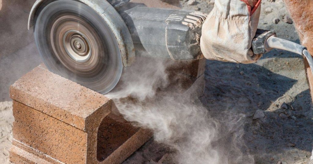 Person cutting cinder block with angle grinder outdoors